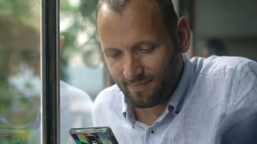 Man with beard looking at phone in bright daylight