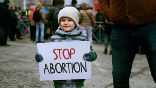 Child Holding Sign in an Urban Crowd