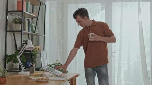 Man Works at Laptop, Drinks Coffee in Home Office