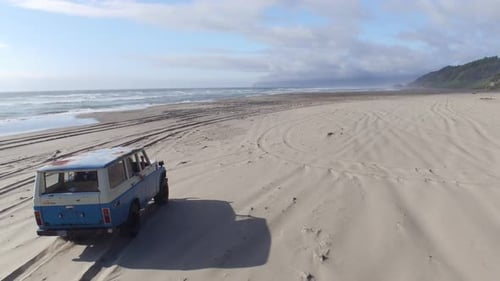 Aerial view of young friends driving a vintage suv on a sunny beach holiday