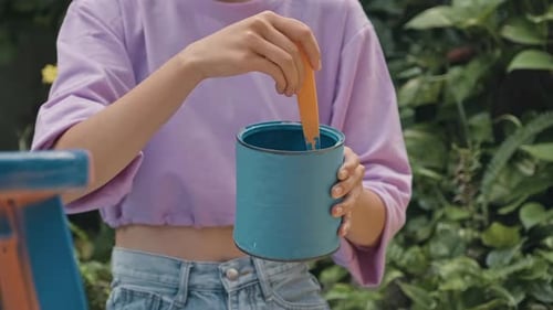 Person Stirring Blue Paint Can in a Garden