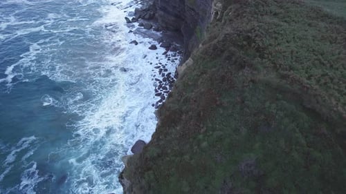 Drone capture the edge of the hill in Isla and also blue Cantabrian sea hitting the rocks from a gre