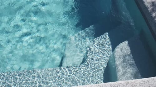 Clear blue water in a private tiled pool with underwater steps and bright sunlight reflections creat