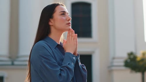 Woman Praying Outdoors in City Sunlight