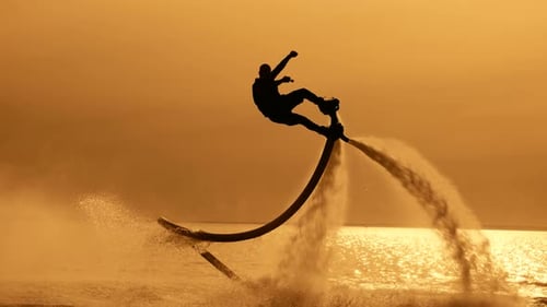A Figure Against a Sunset Sky and Sun An Epic and Beautiful Scene a Flyboarder Flying Over the Water
