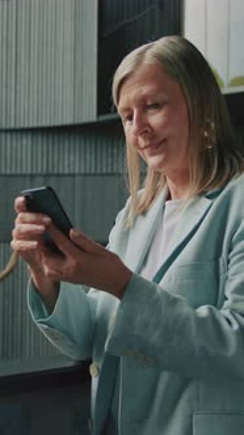 Footage of Grayhaired Smiling Businesswoman in Blue Jacket Big Earrings Chatting on Smartphone