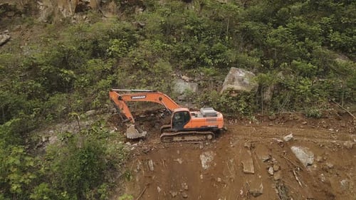 Ein Bagger kippt gekonnt Steine einen Berghang hinunter und zeigt so die Kraft des Schweren in rauem Terrain