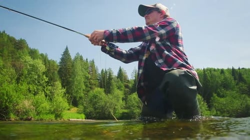 Fly fishing. Angler casts the fly on the rapid river. Fisherman with fly rod fishing on the river