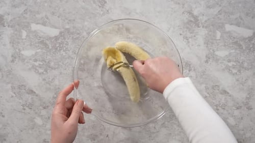Smashing Riped Bananas in a Glass Mixing Bowl to Prepare Coconut Banana Pancakes