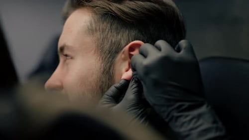 Tattoo piercing studio - a woman makes an ear piercing to a man to a guy