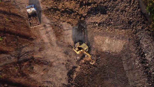 Aerial view of a wheel loader excavator with a backhoe loading sand into a heavy earthmover