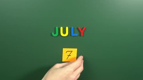 Hand sticking a sticker 7 July calendar day on school board. 7 date of July. Seventh day July