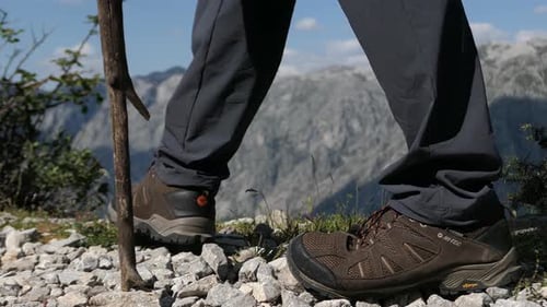 Man hiking in the mountains with trekking shoes and walking stick, closeup