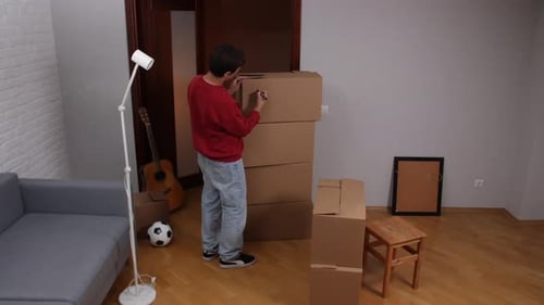 Man Labeling Cardboard Boxes in New Apartment After Moving in