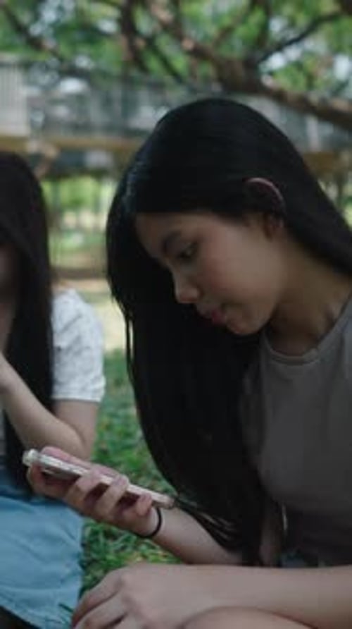 Two Friends are Enjoying Their Time Together in a Park Looking at Their Smartphones