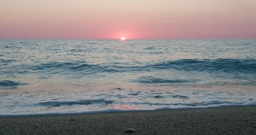 Fundo romântico do pôr do sol no mar. Horizonte de cor roxa, céu sem nuvens e ondas em direção a uma pedra
