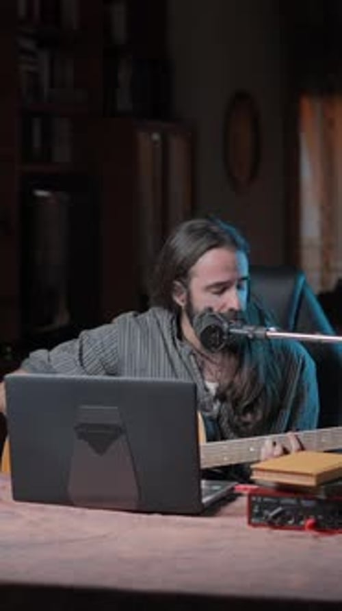 Man playing guitar and singing into microphone at desk