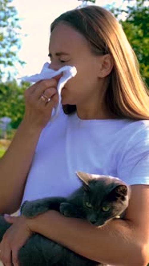 Woman Holding Cat Sneezes Due to Outdoor Allergies