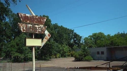 Rotating right pan shot of a rusty retro store sign out front of an abandoned lumber yard and a vint