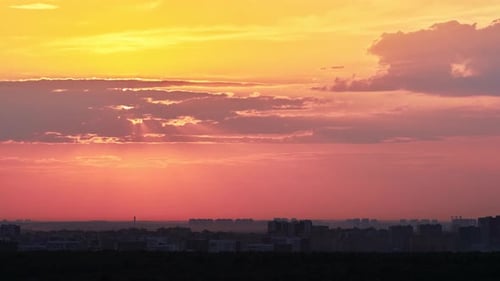 Big red sun over the roofs of city buildings, evening sunset. Timelapse of a cloudy sky and the sun