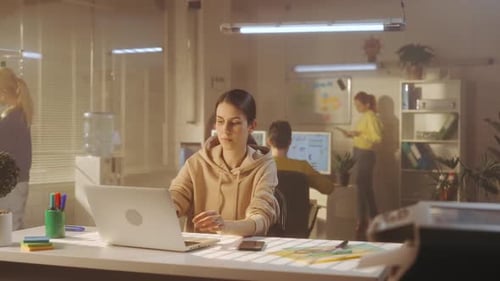 A Young Woman is Typing on a Laptop Keyboard While Sitting at a Table in the Office