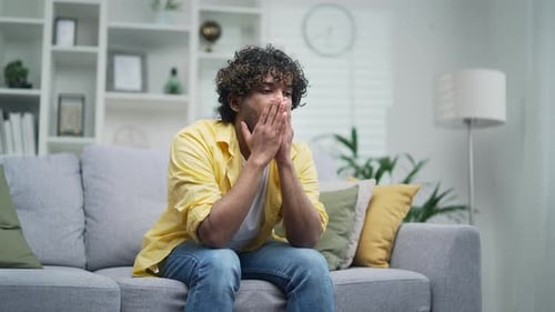 Man with Curly Hair Massaging Face on Couch