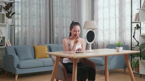 Asian Woman Looks In The Mirror Applying Lipstick Then Smiles While Wearing Makeup