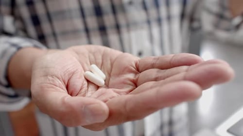 Midsection of senior biracial man at home holding two pills in palm of hand, slow motion