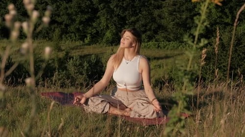 Young Woman Meditating on the Mat Outdoors at Sunset with Beautiful Landscape on the Background
