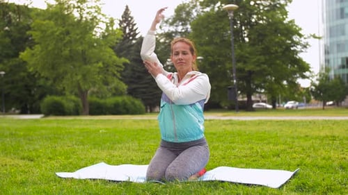 Woman Kneeling Doing Shoulder Stretch in Green Park