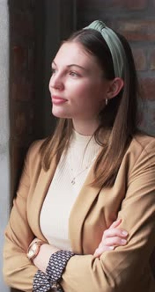 Vertical video: Businesswoman in blazer standing with arms crossed, smiling confidently in office