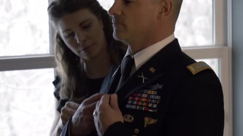Loving Woman Adjusts Military Man's Uniform Indoors