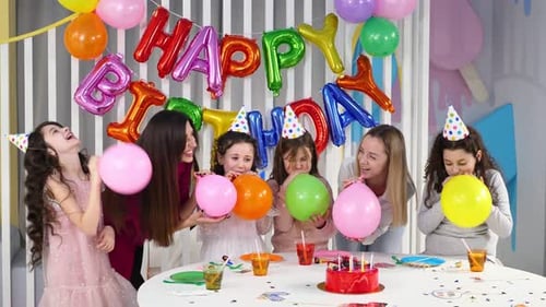 Smiling Children and Women Blow up Balloons at Birthday