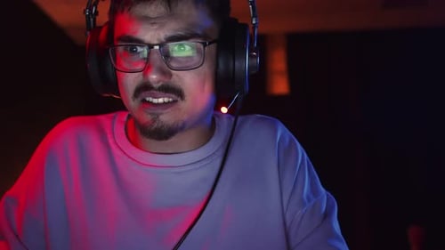 Male Gamer Looks in Surprise at Computer Screen Playing Video Games Front View Man with Glasses is