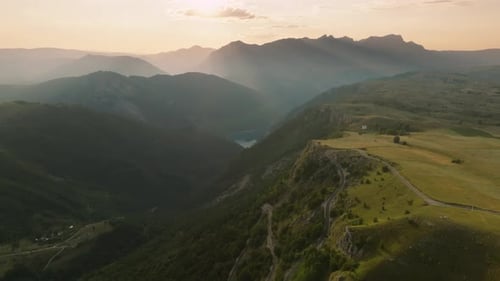 Drone view of a steep winding asphalt road descending in the mountains with mountain backdrop and su
