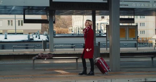 Young Girl with Luggage Walks Along a Departing Train at the Railway Station