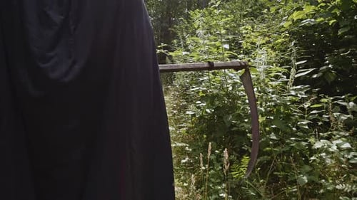 Scythe Carried By Spooky Reaper In Black Hood Outdoor. Horror Concept. medium shot