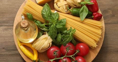 Board with different types of raw pasta and products turning on wooden table, top view
