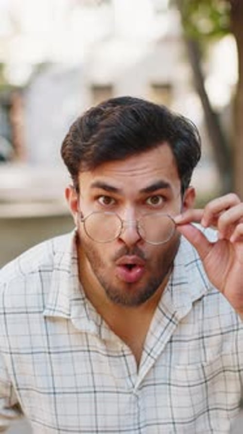 Young Indian Man Looking Surprised at Camera with Big Open Eyes Adjusting Glasses on City Street