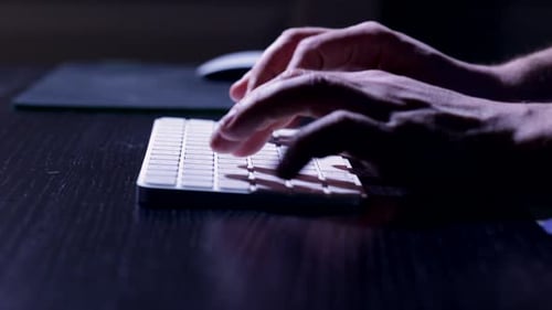Les doigts tapent sur le clavier, illuminés par l'écran de l'ordinateur