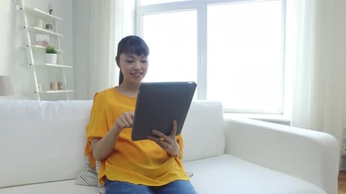 Young Woman Uses Tablet on White Couch at Home