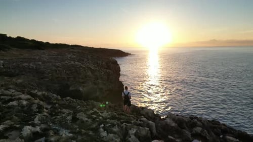 Man With Backpack Standing On Rocky Cliffs During Sunrise Near Sa Coma In Mallorca, Spain. Aerial Dr
