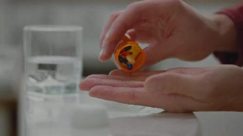 Ein weißer Mann nimmt Pillen, indem er sie aus einer orangefarbenen Flasche auf seine Hand gießt. Einnahme von Pillen auf einem