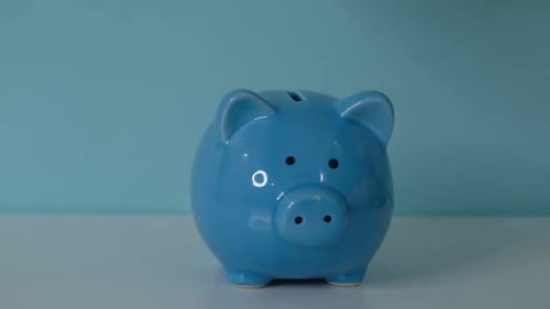 Piggy Bank Business Concept A Hand is Putting a Coin in a Piggy Bank on a Blue Background Saving