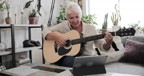 Mujer adulta madura aprendiendo a tocar la guitarra en casa con un vídeo tutorial