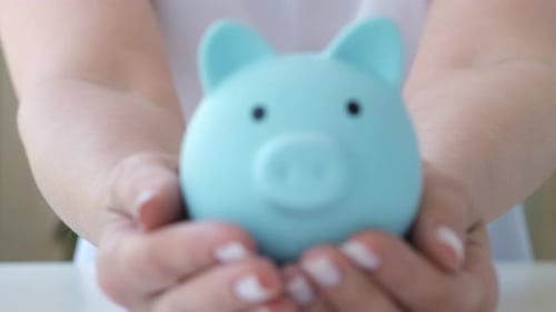 Female Hands Holding Blue Piggy Bank on White Table Saving Money Concept