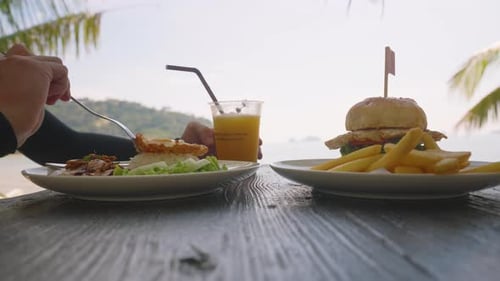 Man Eating Chicken Rice and Burger Meal While Drinking Smoothie at Beach Table with Sea View Fast Fo