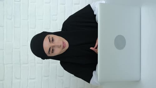 Woman in head covering has video call with laptop