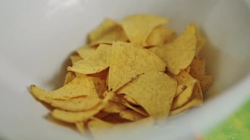 Yellow Corn Chips Fall into White Bowl in Realistic Handheld Close Up Shot