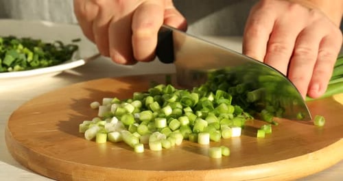 Woman cutting green onions at table, closeup